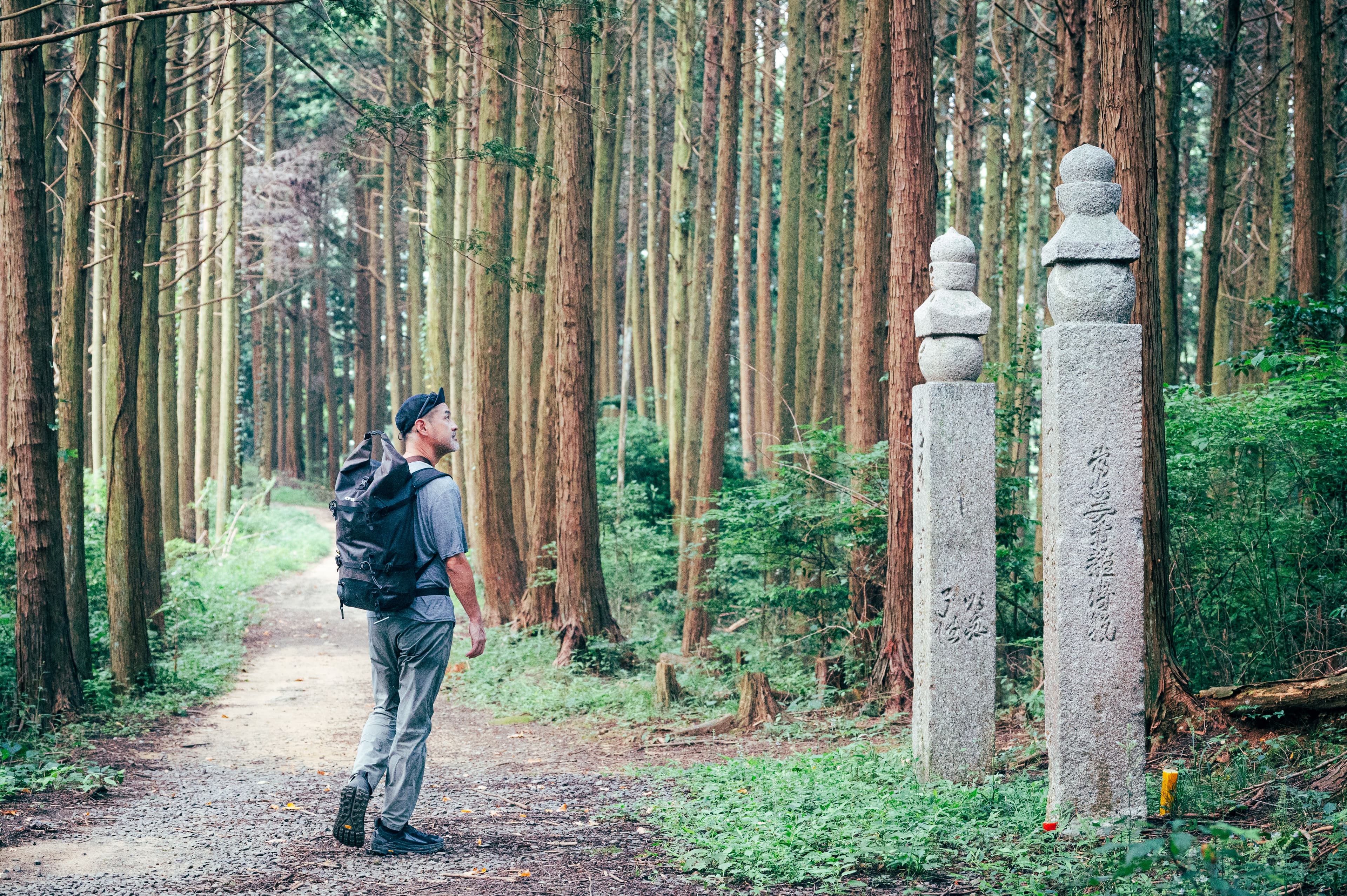 Hiker on a forest trail past traditional stone pillars